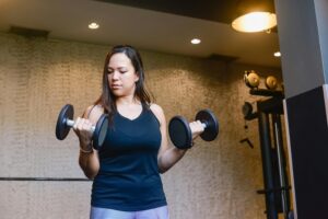 A woman in activewear lifting dumbbells indoors, focused on her workout routine.