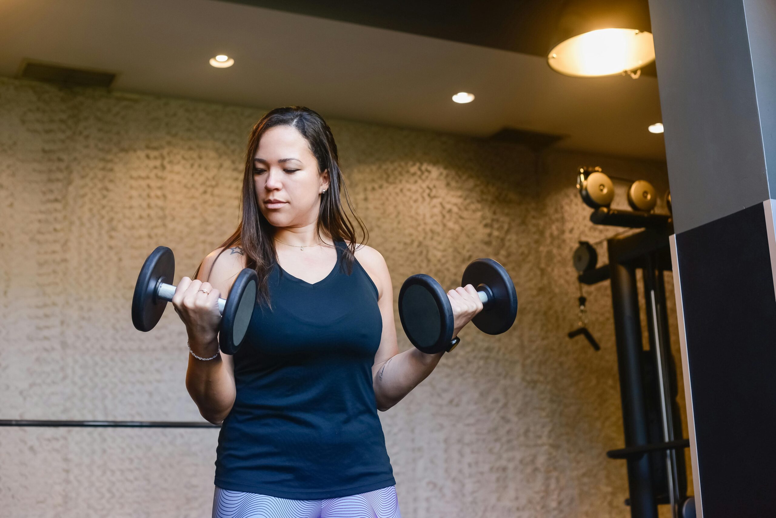 🏃♀️ Como treinar de acordo com o biotipo feminino e ter melhores resultados A woman in activewear lifting dumbbells indoors, focused on her workout routine.